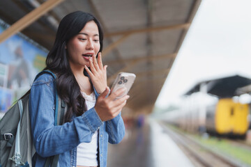 Young woman expressing surprise while reading a message on smartphone at train station