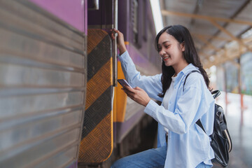 Young woman boarding train using smartphone at station