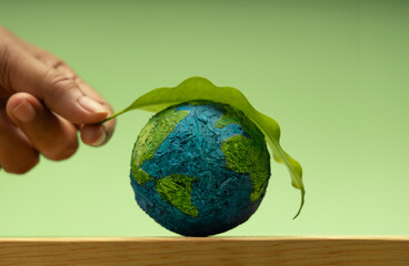 Hand putting Green leaf on Earth. Environmental sustainability, Earth Day, global ecological care and Healthy planet Globe