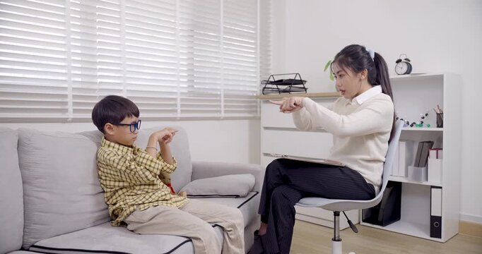 asian boy sitting on sofa pointing back at psychologist during child therapy session expressing reaction and participation in behavioral counseling for adhd management and trust building
