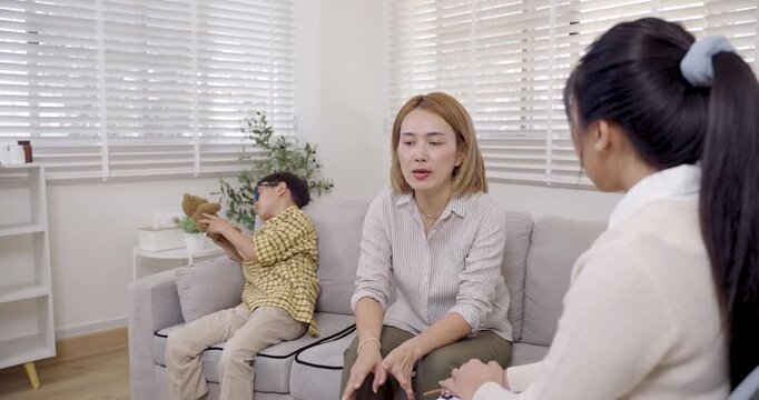 Asian single mother expresses frustration while sitting on sofa as female psychologist calmly listens and explains during therapy session about managing child adhd behavior and emotional stress