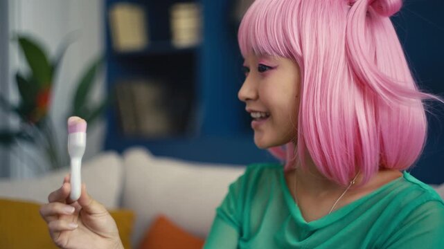 Asian woman with pink hair applying makeup with brush, recording beauty video