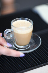 A Delicious Hot Espresso Coffee Drink Served in a Clear Glass Cup with a Handle on a Saucer with a Hand Reaching for It