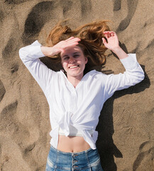 top view of young woman lying on sand enjoying vacation , covering face with hand