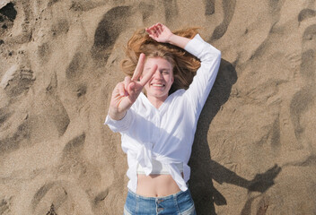top view of young woman lying on sand enjoying vacation , showing peace gesture