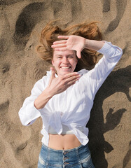 top view of young woman lying on sand enjoying vacation , making frame sign with hands