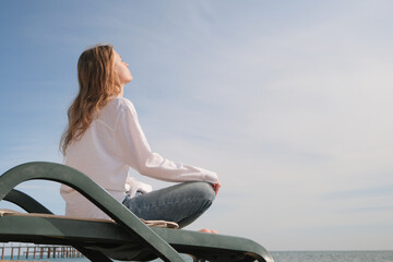 young woman sitting in the chaise lounge on the edge of the sea