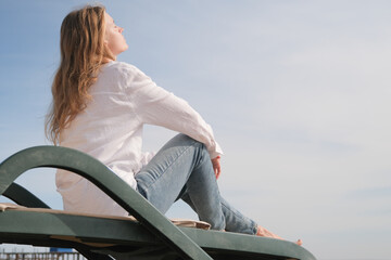 young woman sitting in the chaise lounge on the edge of the sea