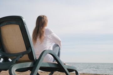 young woman sitting in the chaise lounge on the edge of the sea