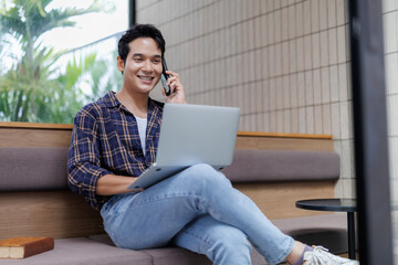 Young man working remotely using laptop and talking on phone