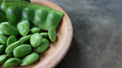 Fresh petai or stink beans in wooden plate on cement background