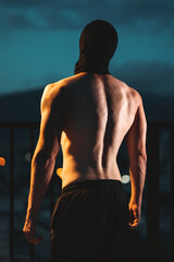 Muscular athlete with perfect physique posing from back at night, strength and dedication, Toned man with ideal body power and discipline in evening silhouette