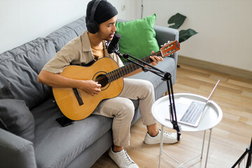 Young Male Musician Singing And Playing Acoustic Guitar Into Microphone At Home