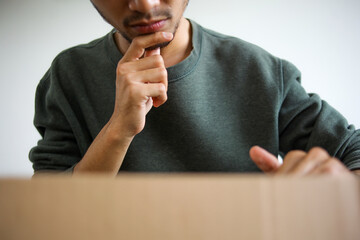Young Asian Man Appearing To Ponder Or Evaluate The Contents Of Newly Delivered Package