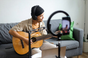 Young Man In Headphones Playing Guitar And Singing Into Microphone For Online Audience