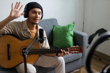 Young Male Musician Waving To Audience While Playing Guitar And Recording Music At Home