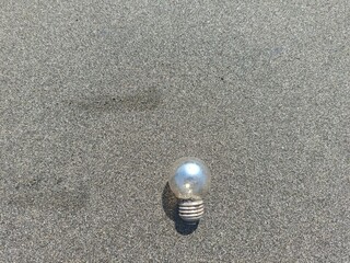 An old light bulb lying on the black sand beach in Jembrana, Bali, symbolizing ocean waste and environmental concerns.
