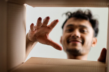 Happy Male Customer Looking Down Into Package Reaching For Contents During Unboxing