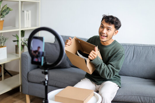 Joyful Asian Male Influencer Unboxing Package For His Live Video