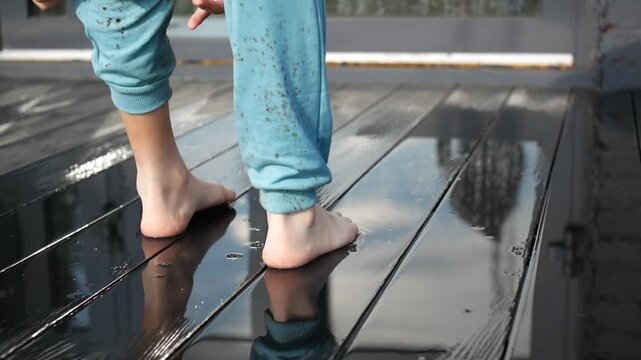 Close-up of barefoot child standing on a rain-soaked porch