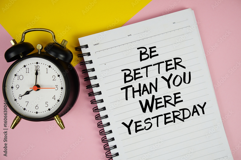Poster be better than you were yesterday text written on notepad with alarm clock on pink background