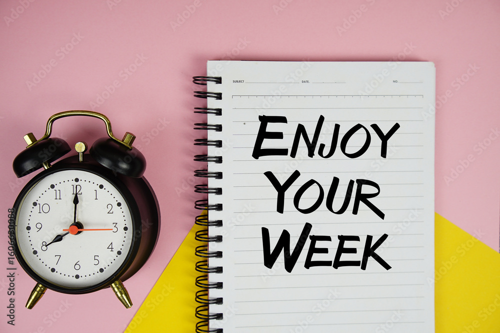 Poster enjoy your week text written on notepad with alarm clock on pink background