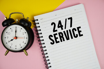 24 Hrs 7 Day Service text written on notepad with alarm clock on pink background