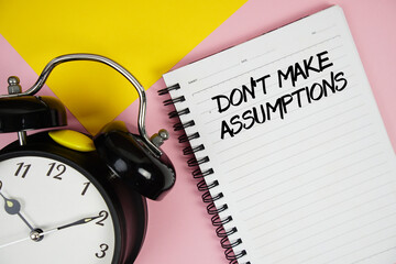 Don't Make Assumptions text written on notepad with alarm clock on pink background