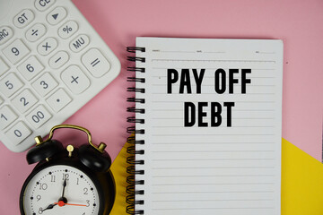 Pay Off Debt text written on notepad with calculator and alarm clock on pink background