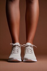 Stylish sneakers on toned legs against warm, neutral background