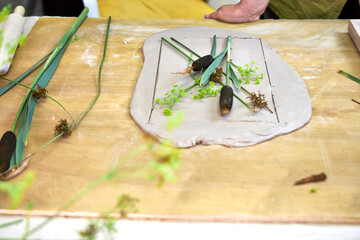 Placing fresh flowers and leaves on soft clay to create an imprint for plaster relief. Hands...