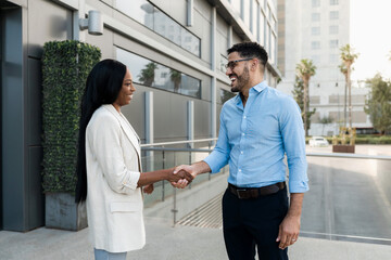 Two smiling diverse business people shaking hands outside office after reaching an agreement