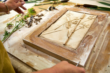Hands holding finished botanical plaster relief in a wooden frame. DIY floral artwork with imprints...