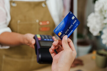 Asian older florist holding payment terminal receiving credit card from customer for flower shop purchase showing electronic transaction and contactless cashless payment method