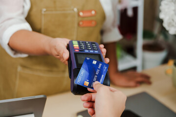Senior asian florist handing credit card terminal to customer receiving electronic payment inside flower shop symbolizing cashless commerce and digital transaction in small business