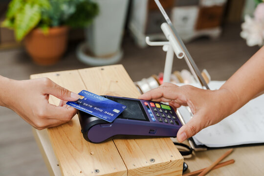 Card being swiped through reader placed on counter during purchase at floral shop managed by asian senior woman offering contactless payment for bouquet and flower items - Powered by Adobe