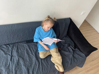 Kid little girl sitting on sofa reading book at home. Childhood and people concept