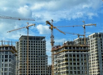 Tower cranes construct buildings under a blue sky dotted with white clouds.
Concept of: Urbanization.