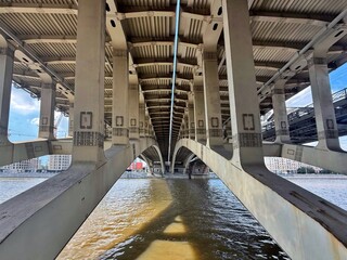 An upward view showcases the intricate underside of a bridge arching over a river. Concept of: Architectural symmetry.