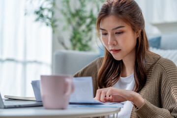 woman sitting at table, reviewing documents with focused expression. soft pink mug is placed...
