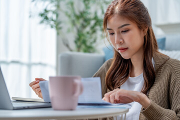 Focused woman reading documents at home with laptop and coffee
