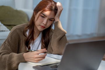 Struggling woman studying at home, taking notes with laptop nearby