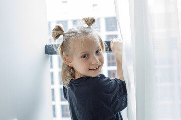 Happy child girl standing at the window at home
