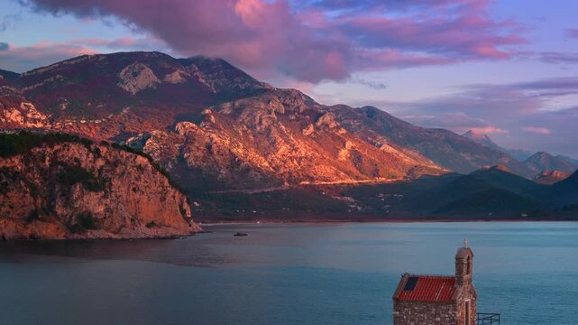 Aerial drone view of stunning sunset over the mountains and tranquil waters of a coastal Sveta Nedjelja Island in Petrovac, Montenegro