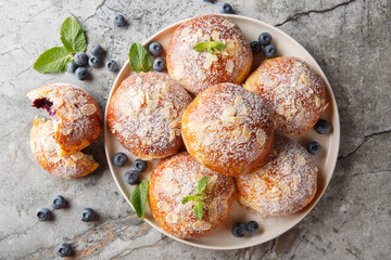 sweet buns with fresh blueberries and almond petals and powdered sugar close-up in a plate on the table. Horizontal top view from above