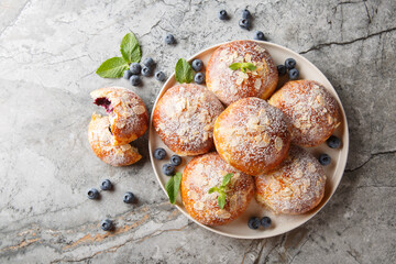 Yeast buns with blueberries, almond petals and powdered sugar close-up in a plate on the table. Horizontal top view from above