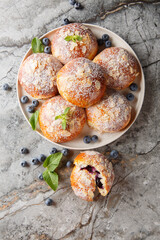 Close-up of brioche buns with blueberries, almond flakes and powdered sugar in a plate on the table. Vertical top view from above