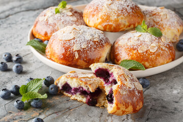 sweet buns with fresh blueberries and almond petals and powdered sugar close-up in a plate on the table. Horizontal