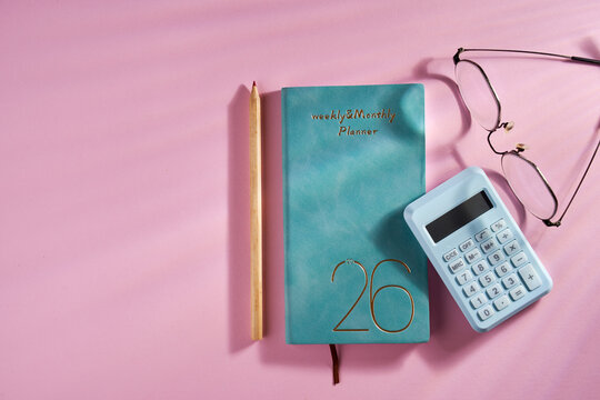 2026 planner, calculator, eyeglasses and pencil  against pink background.