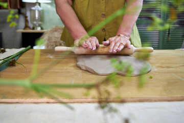 Rolling out clay sheet with a rolling pin to prepare base for plaster relief with flowers. Hands...